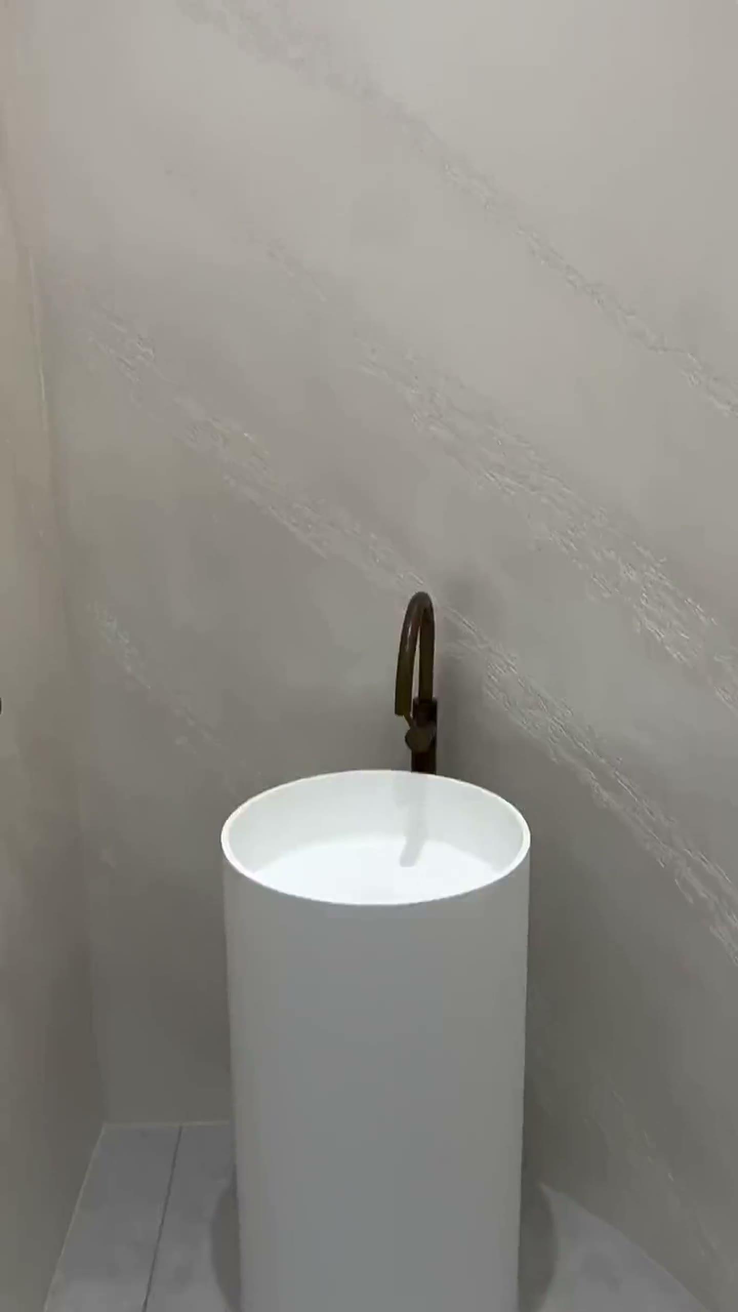 Pale Pietra Spaccata with a mother-of-pearl shimmer curving into the ceiling above a cylindrical basin and bronze tapware