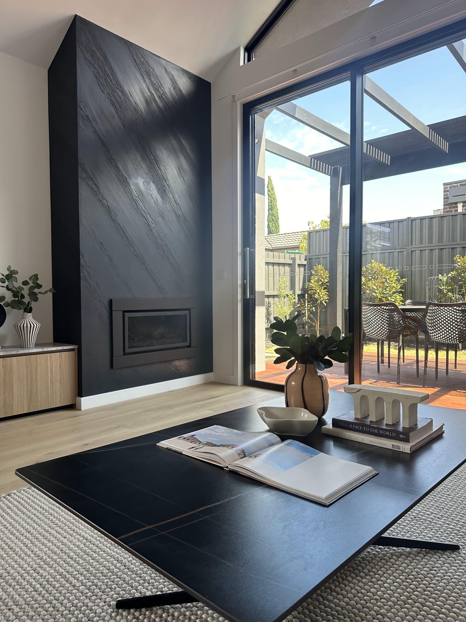 A full-height charcoal plaster chimney breast with a linear gas fire set into it, beside sliding doors onto a deck