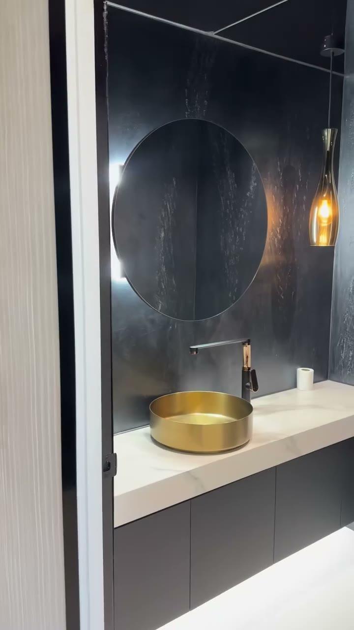 A powder room finished in dark burnished plaster, the sheen shifting across the wall behind a round mirror, brass basin and glass pendant