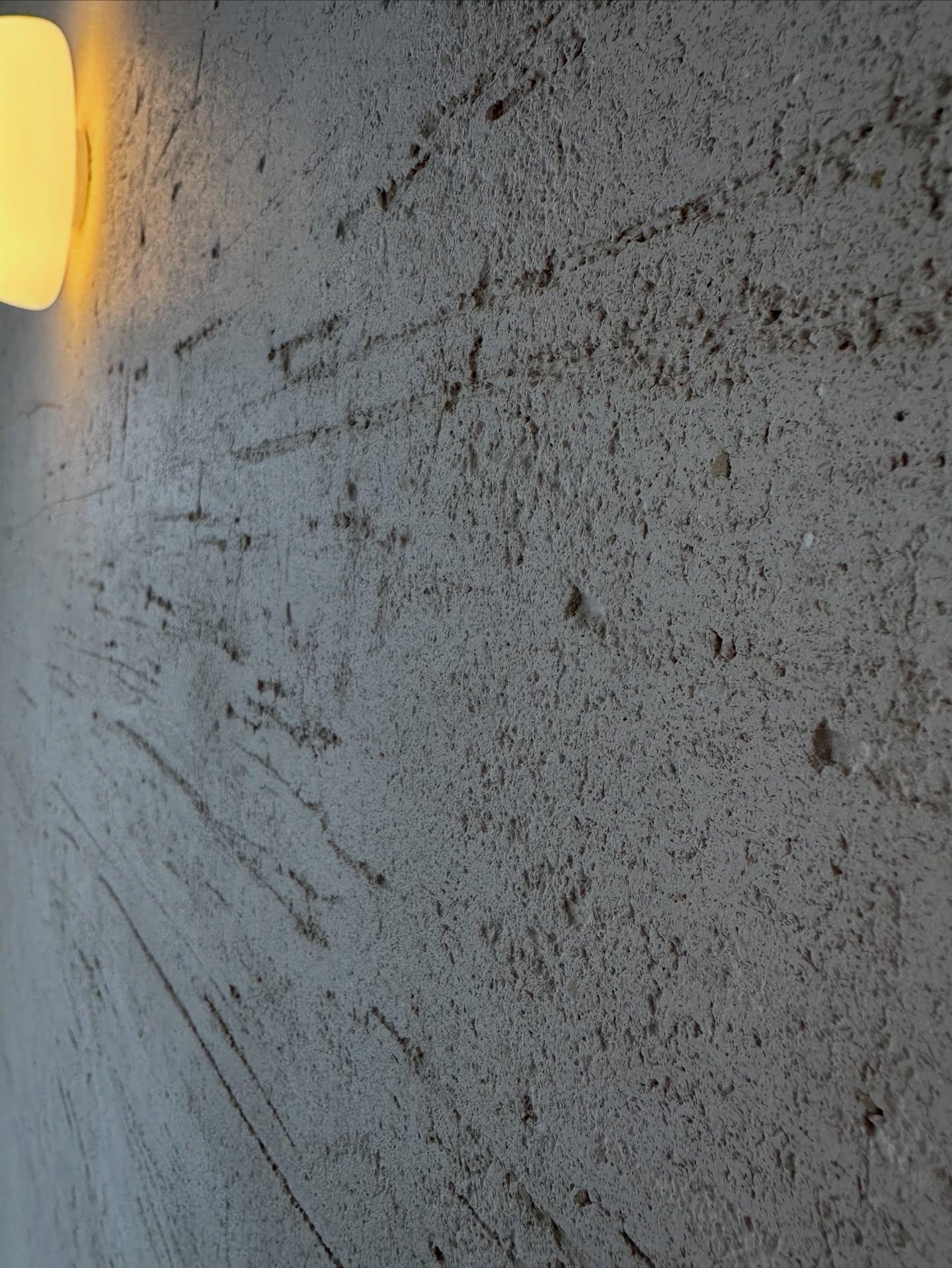 Travertino close up in raking light from a wall lamp, its open voids and horizontal banding reading as the cut face of quarried travertine