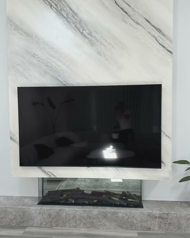 A white split-stone plaster wall with grey veining running diagonally through it, carrying a mounted television above a long gas fire, the wall curving away at its far end