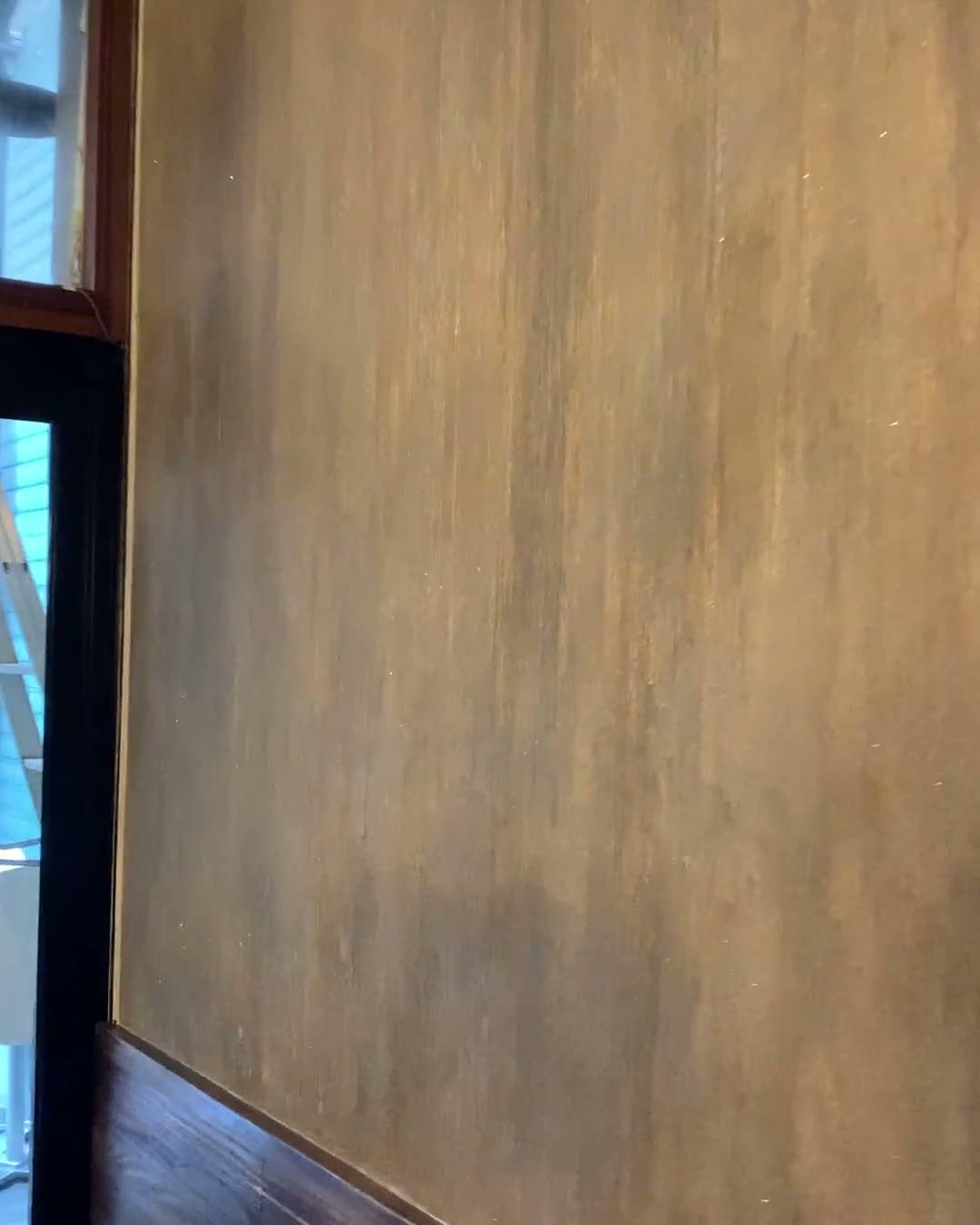 A slow pan along the Brown Sugar wall in bronze-gold burnished plaster, the vertical trowel movement catching the light from the doorway as the camera travels
