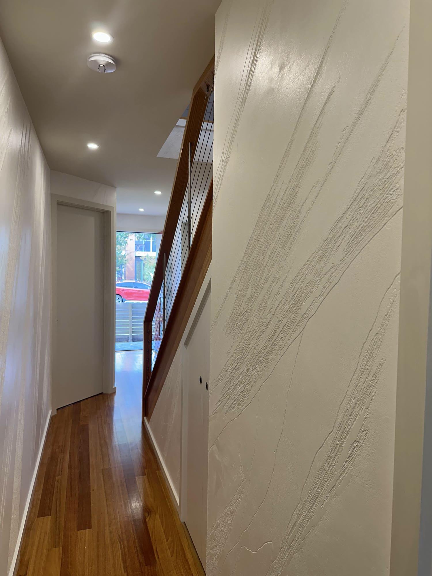 A hallway feature wall in pale plaster with broad sweeping trowel movement through it, above a timber floor